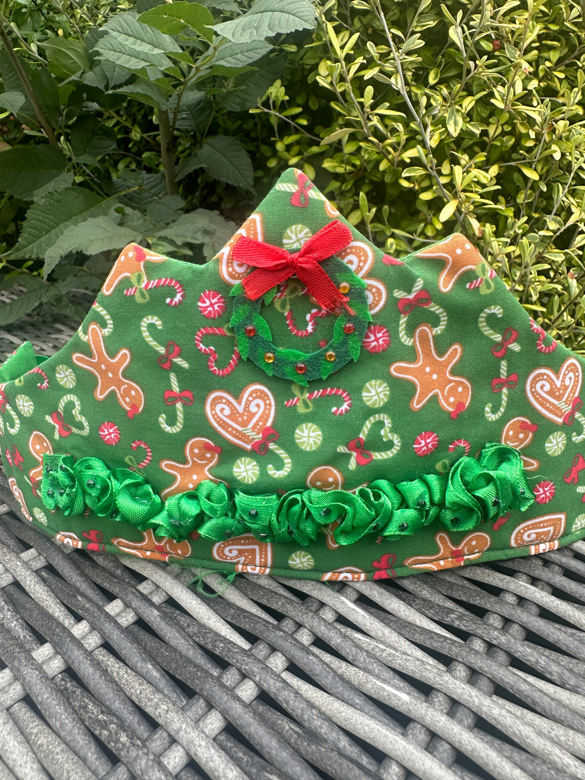 Full view of a green festive Christmas crown with ruffle trim and Christmas wreath embellishment