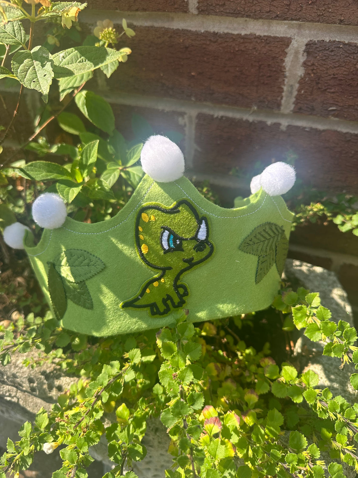 Handmade green dinosaur crown with embroidery and white pompoms