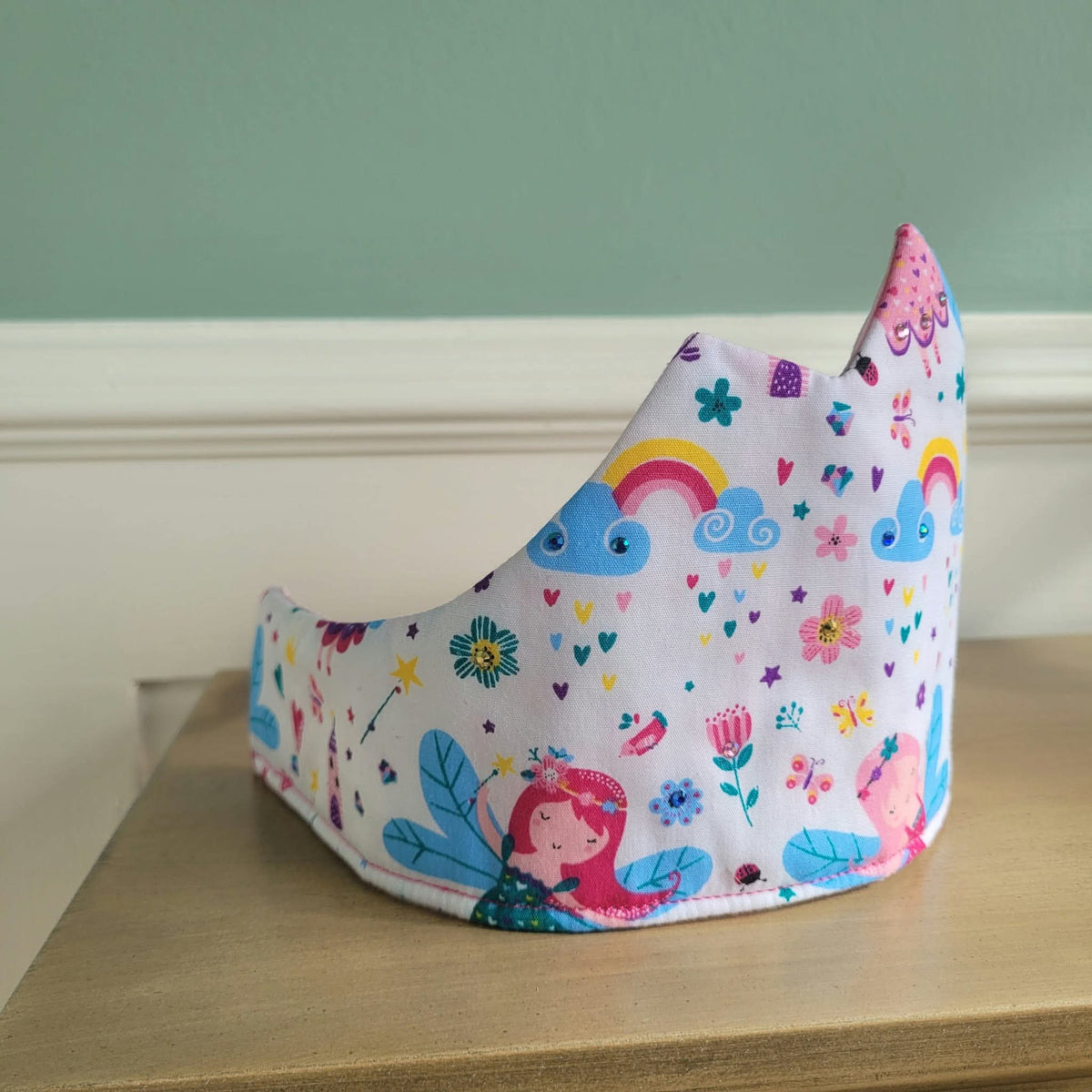 Angled view of pointed fairy-print crown with colourful rainbow and flower motifs