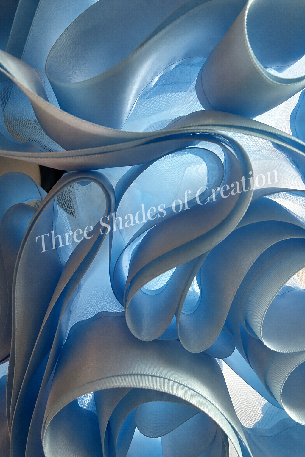Baby blue satin ribbon close-up with translucent Three Shades of Creation watermark