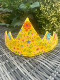 Bright yellow floral crown with colourful fabric flowers displayed on a garden table