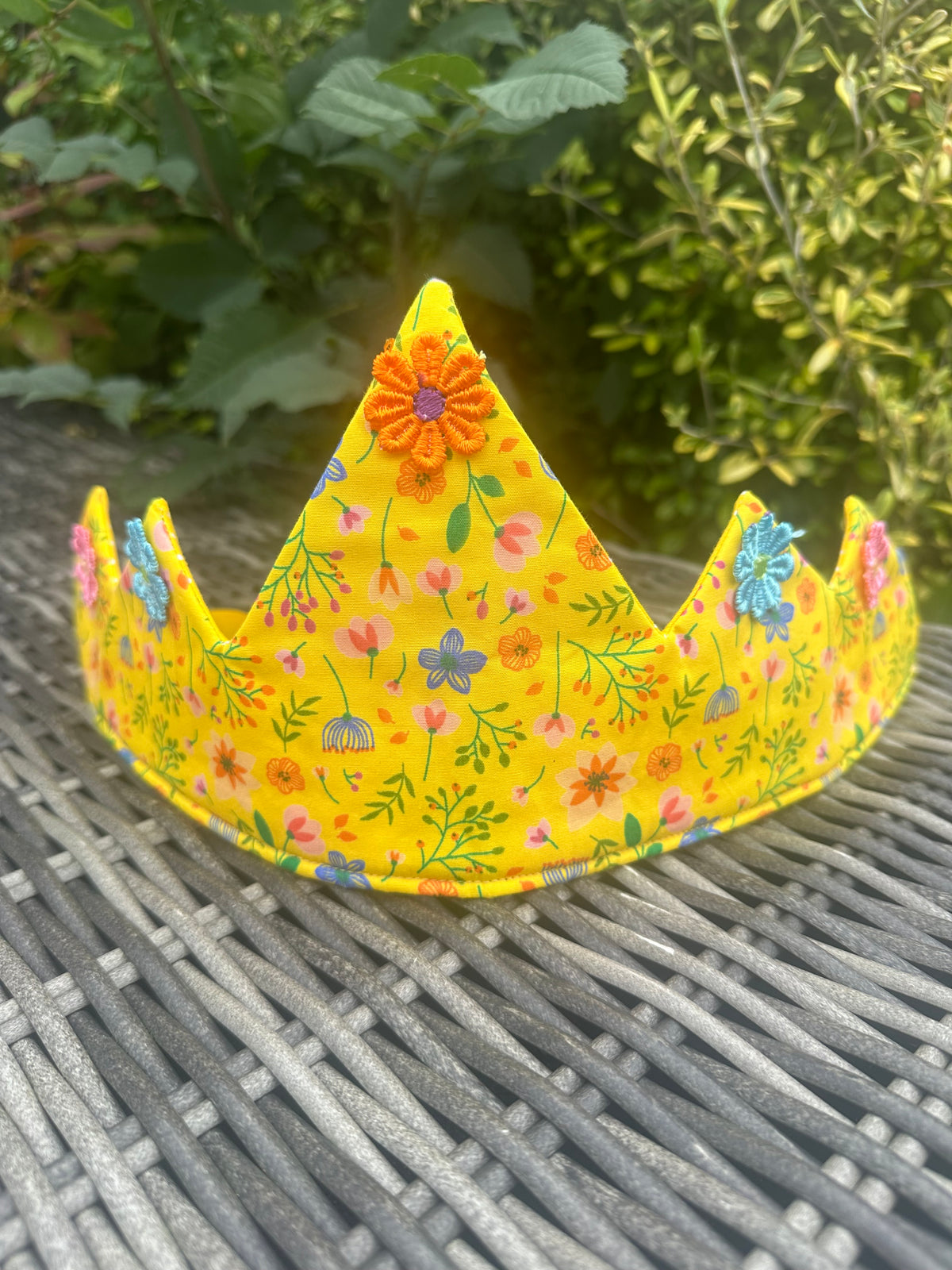 Bright yellow floral crown with colourful fabric flowers displayed on a garden table