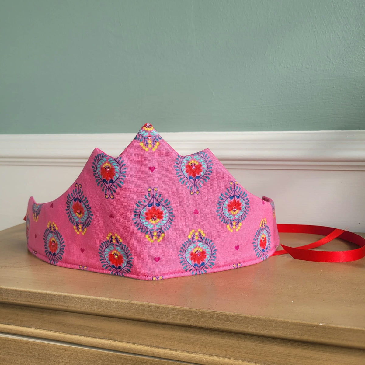 Pink patterned fabric crown shown with red ribbon tie