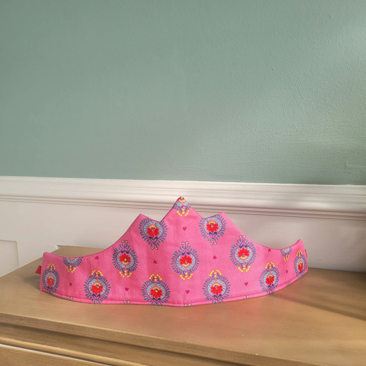 Pink pointed fabric crown with colourful floral-inspired motifs