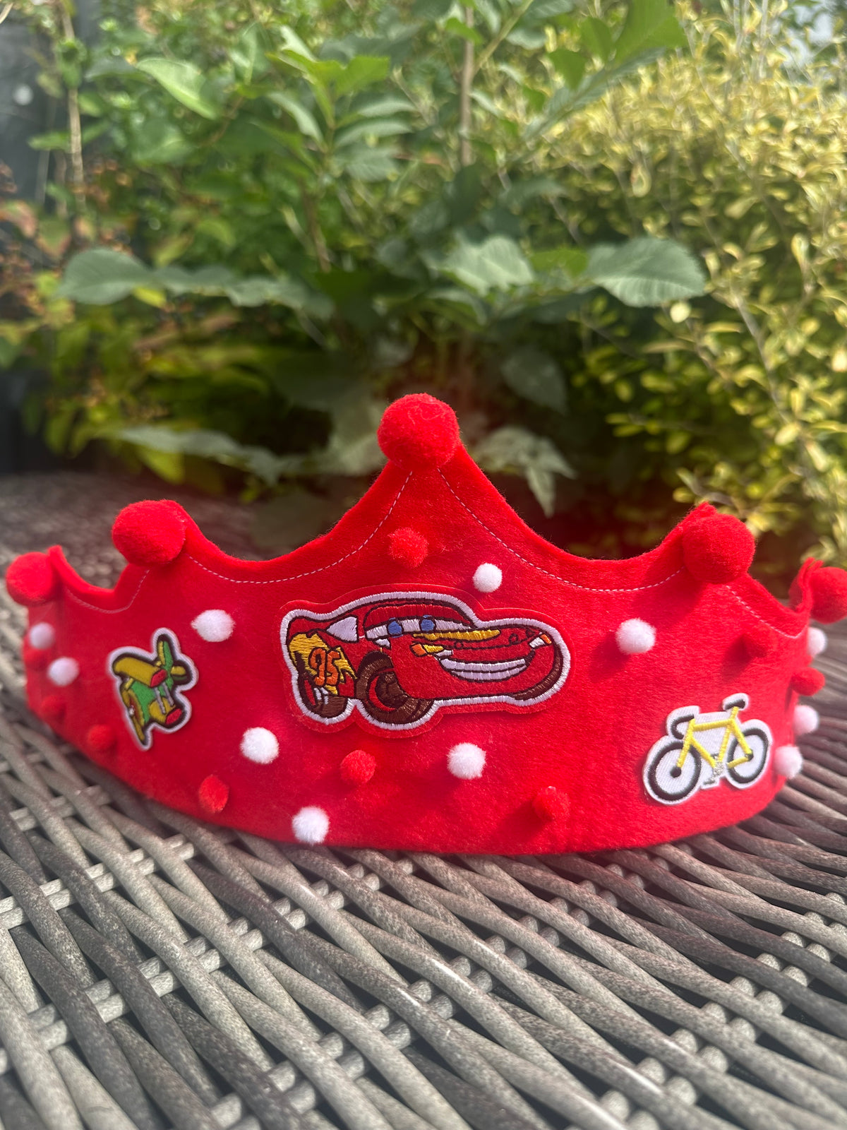 Red felt crown with white pompoms and embroidered racing car, skateboard and bicycle patches
