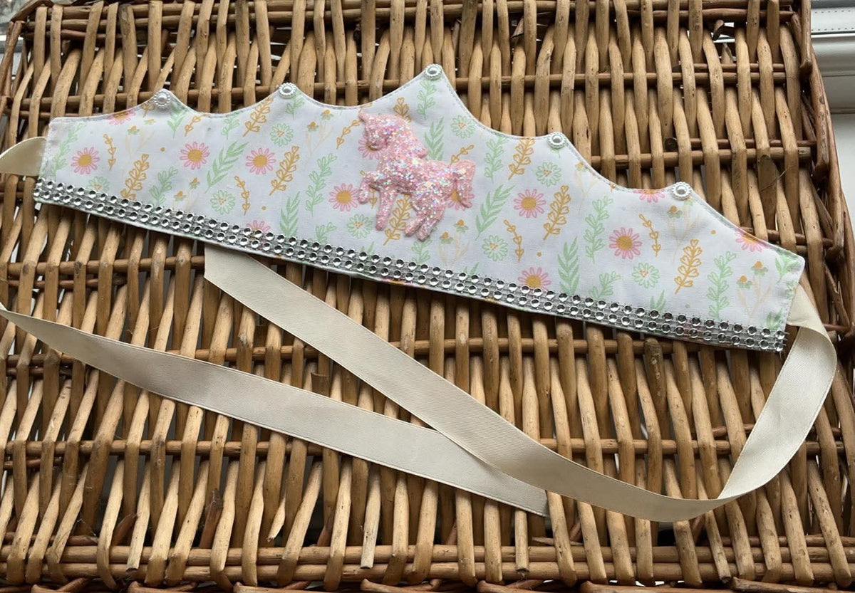 Handmade white floral fabric crown with pink glitter unicorn appliqué, silver rhinestone trim and cream satin ribbon ties
