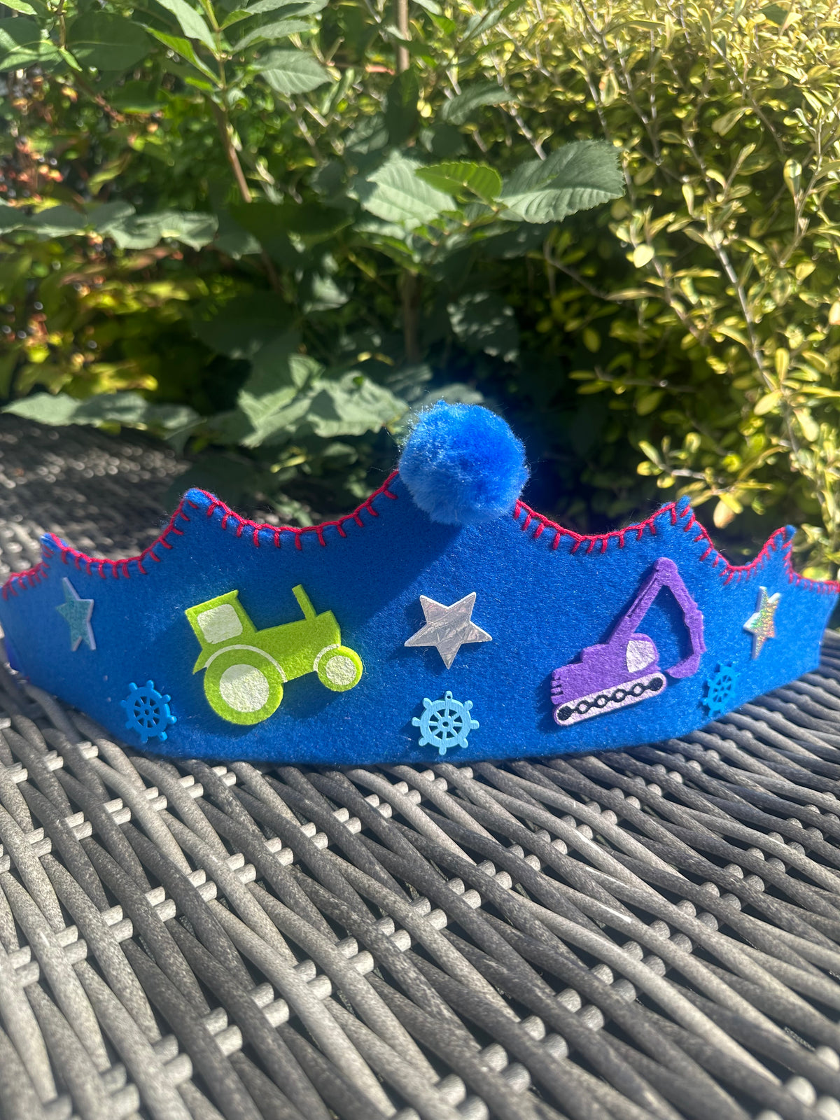 Royal blue felt crown with green tractor, purple digger patches, red blanket stitch edging and blue pompom